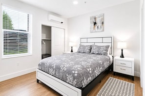 Een slaapkamer met een bed, nachtkastjes, een lamp, een schilderij, een kledingkast en een airconditioning.