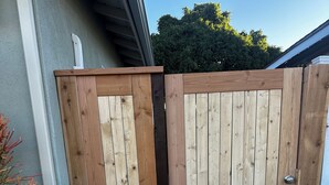 Een houten poort met een metalen hendel, die uitkomt op een pad van bakstenen.
