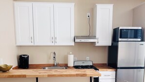Een moderne keuken met witte kastjes, een houten aanrecht, een inbouwmagnetron, een roestvrijstalen koelkast en twee zwarte barkrukken.