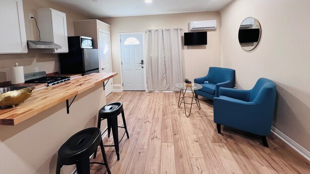 Een gezellige, compacte leefruimte met een kitchenette, een blauwe bank, een kleine tafel en een aan de muur bevestigde televisie.