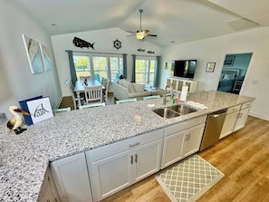 A modern kitchen with granite countertops, white cabinetry, a built-in dishwasher, and a dining area with a table and chairs.