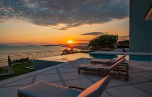 A poolside area with lounge chairs, a view of the sunset over the sea, and a clear sky. - Amazing home in Gornja Podstrana with sauna (Gornja Podstrana)