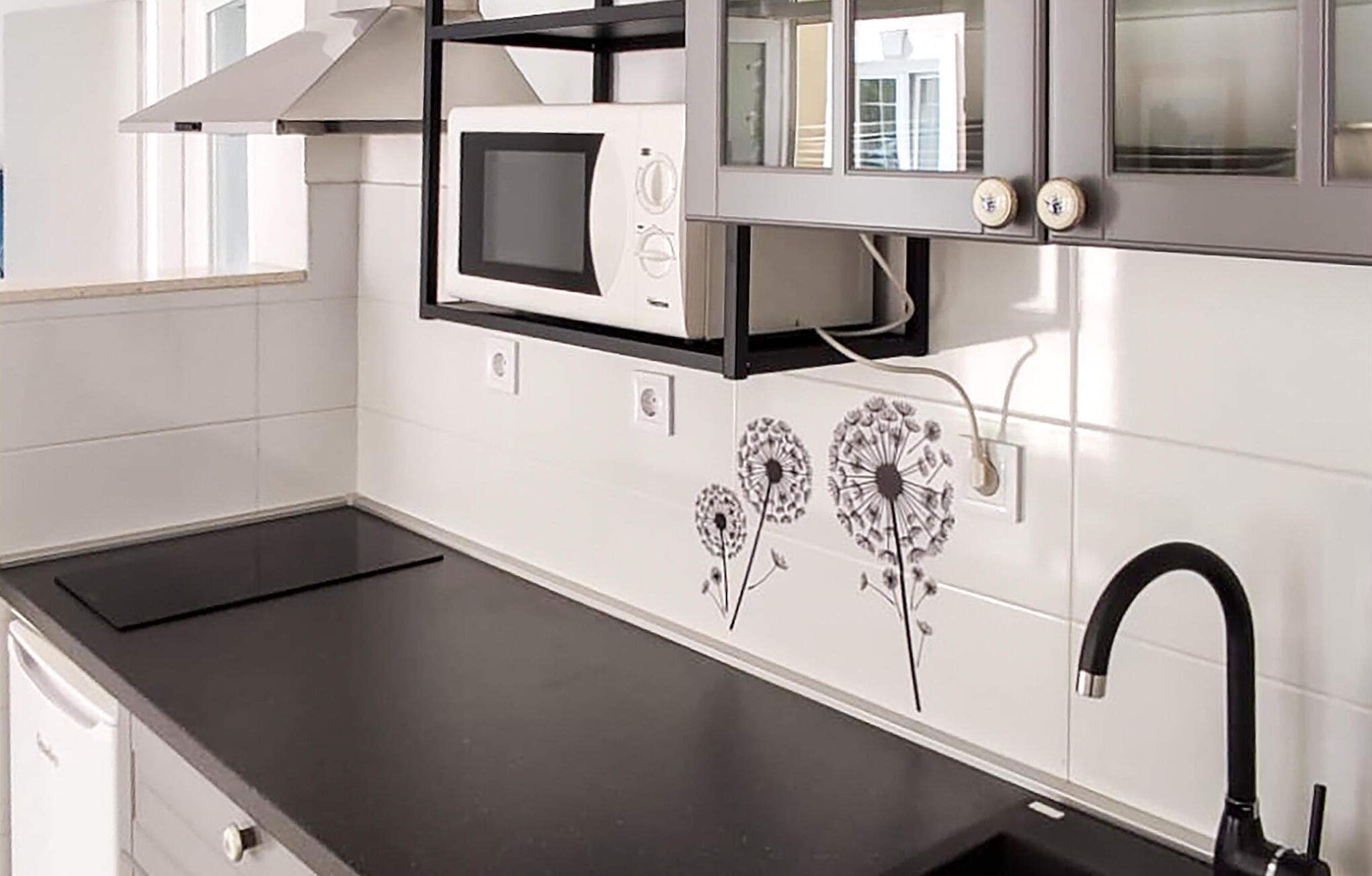A kitchen with a black countertop, a white microwave, and a black faucet.