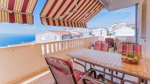 Un balcón con toldos a rayas, una mesa con sillas y vistas al mar y edificios.