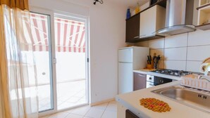 Cocina con estufa a gas, refrigerador y lavamanos. Hay una puerta corrediza de vidrio que da a un balcón.