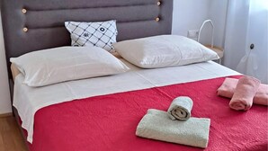 Una cama bien hecha con una colcha roja, dos almohadas blancas y un cabecero gris.