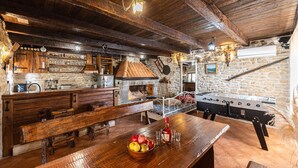 Una cocina rústica con vigas de madera, paredes de piedra, un horno de piedra y una zona de bar con un cuenco de fruta y una botella de licor.