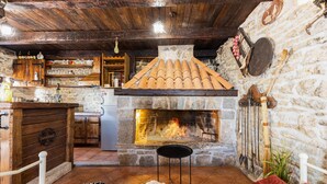 Un interior rústico con chimenea de piedra, vigas de madera y una zona de cocina con estantes y un refrigerador.