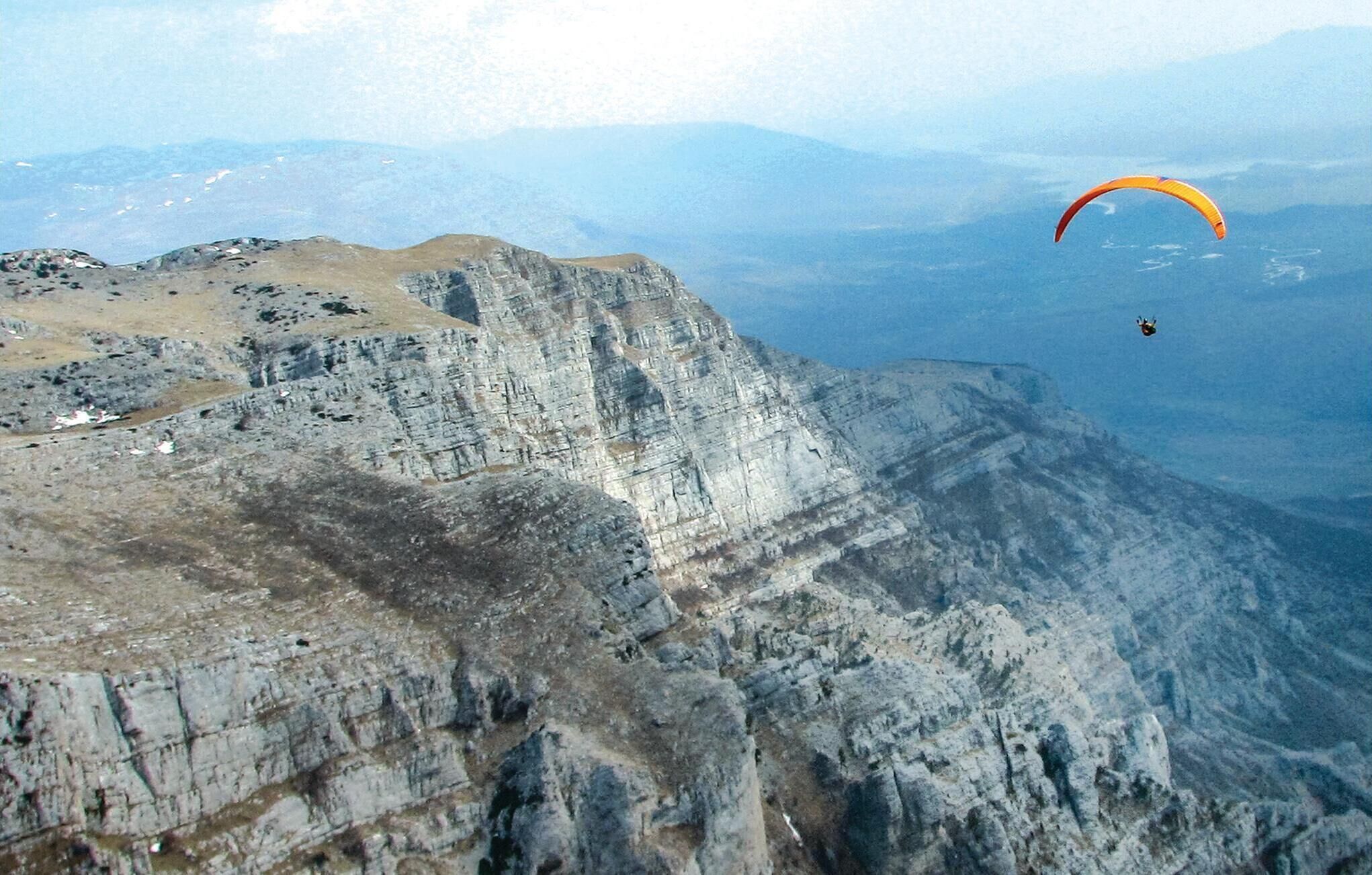 Paisaje montañoso con una persona practicando parapente.