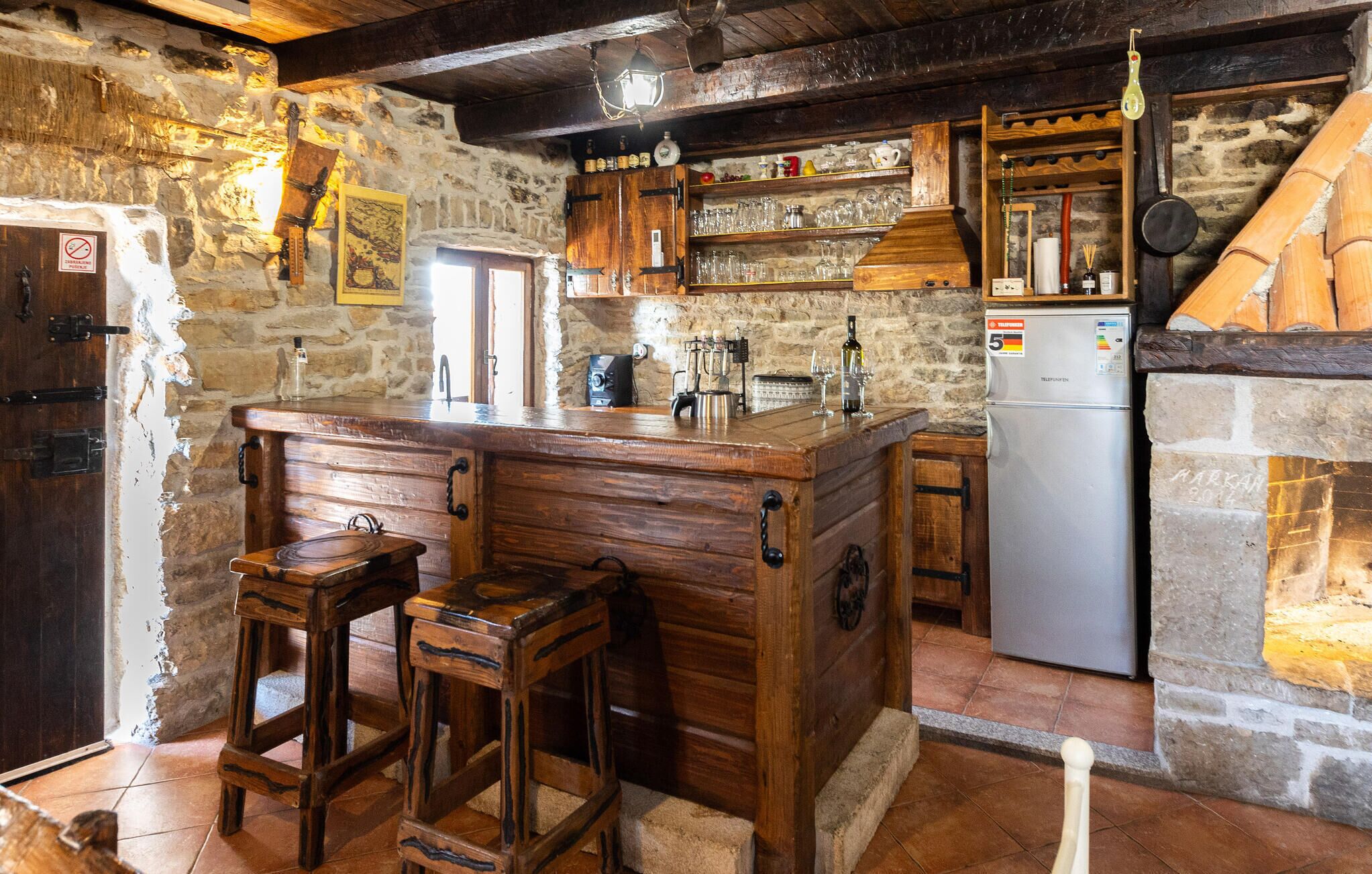 Une cuisine rustique avec des tabourets de bar en bois, un réfrigérateur et des murs en pierre.