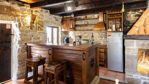 Una cocina rústica con taburetes de madera, un refrigerador y paredes de piedra.