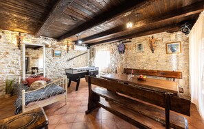 A rustic room with stone walls, a wooden ceiling, a bed with patterned bedding, a foosball table, and a bench. - Amazing home in Donji Bitelic (Donji Bitelic)