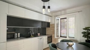 Et moderne køkken med hvide skabe, et sort emhænde og et spiseområde med et rundt bord og grønne stole.