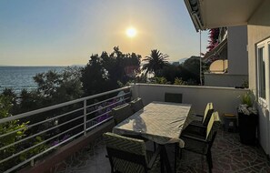 Un balcon avec une table et des chaises, donnant sur une étendue d’eau et des arbres.