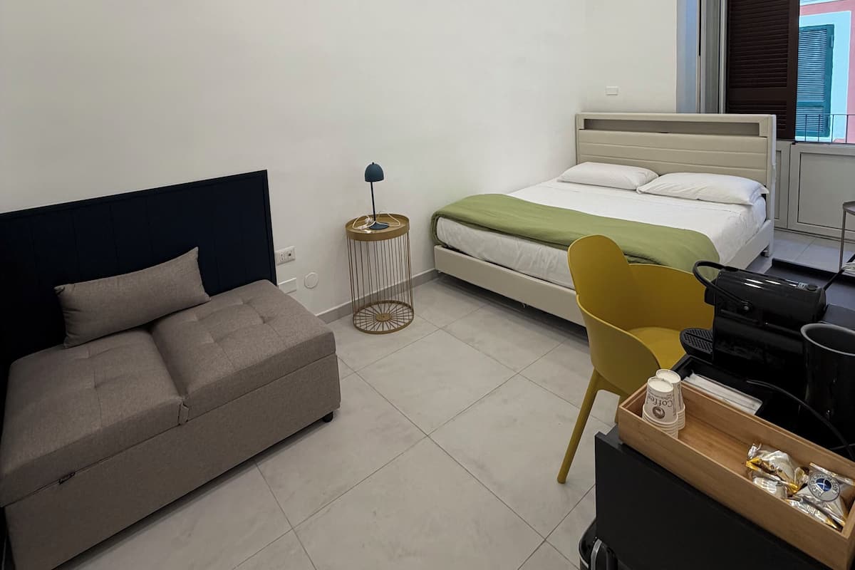Un dormitorio moderno con una cama, un sofá, una mesita auxiliar y un escritorio con una cafetera.