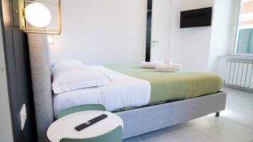 Une chambre d’hôtel moderne, équipée d’un lit, d’une petite table ronde, d’un téléviseur fixé au mur et d’une fenêtre avec des stores.