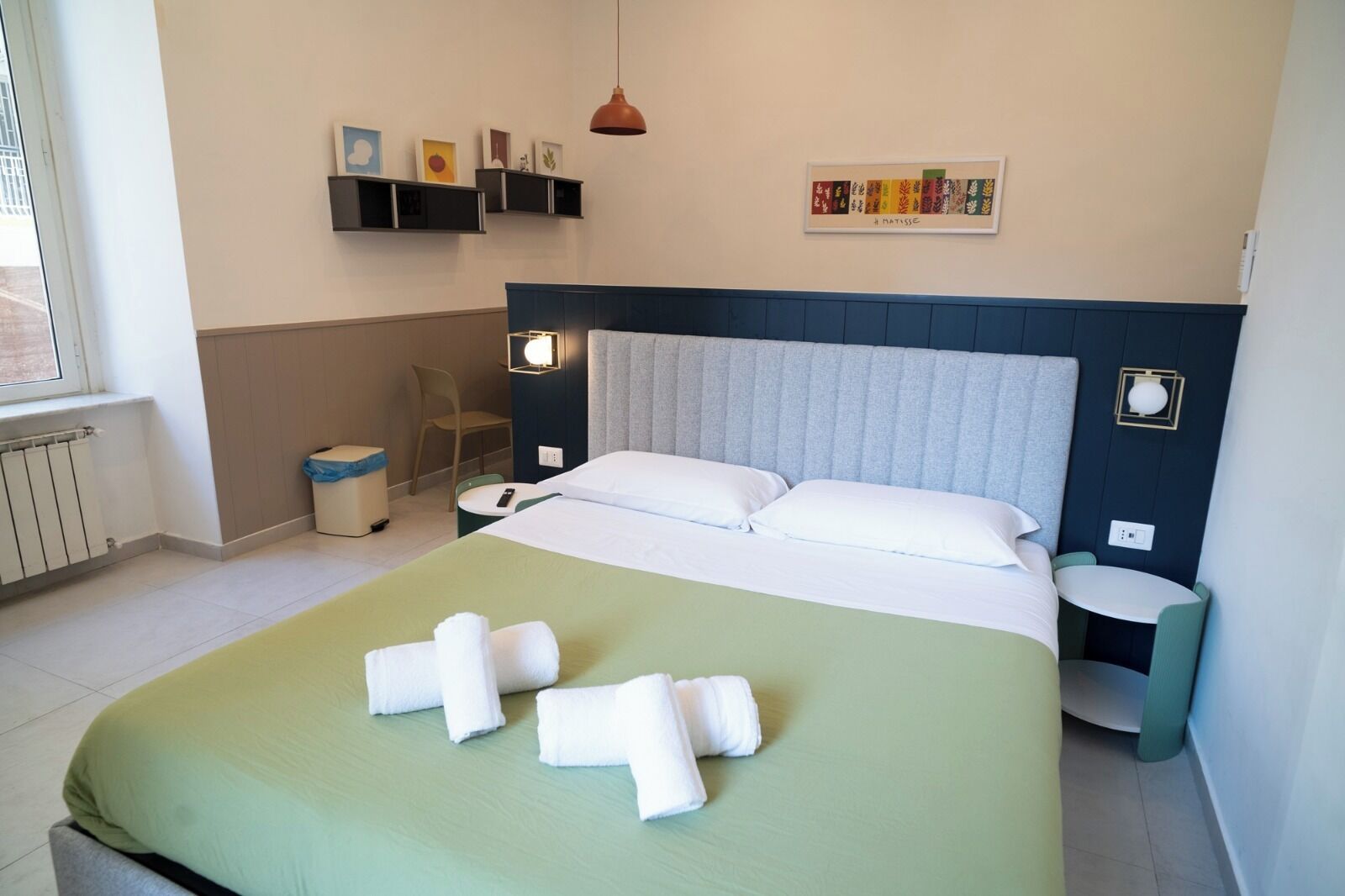 A neatly made bed with white linens and towels, a bedside table with a lamp, a chair, and a small table with a remote control.