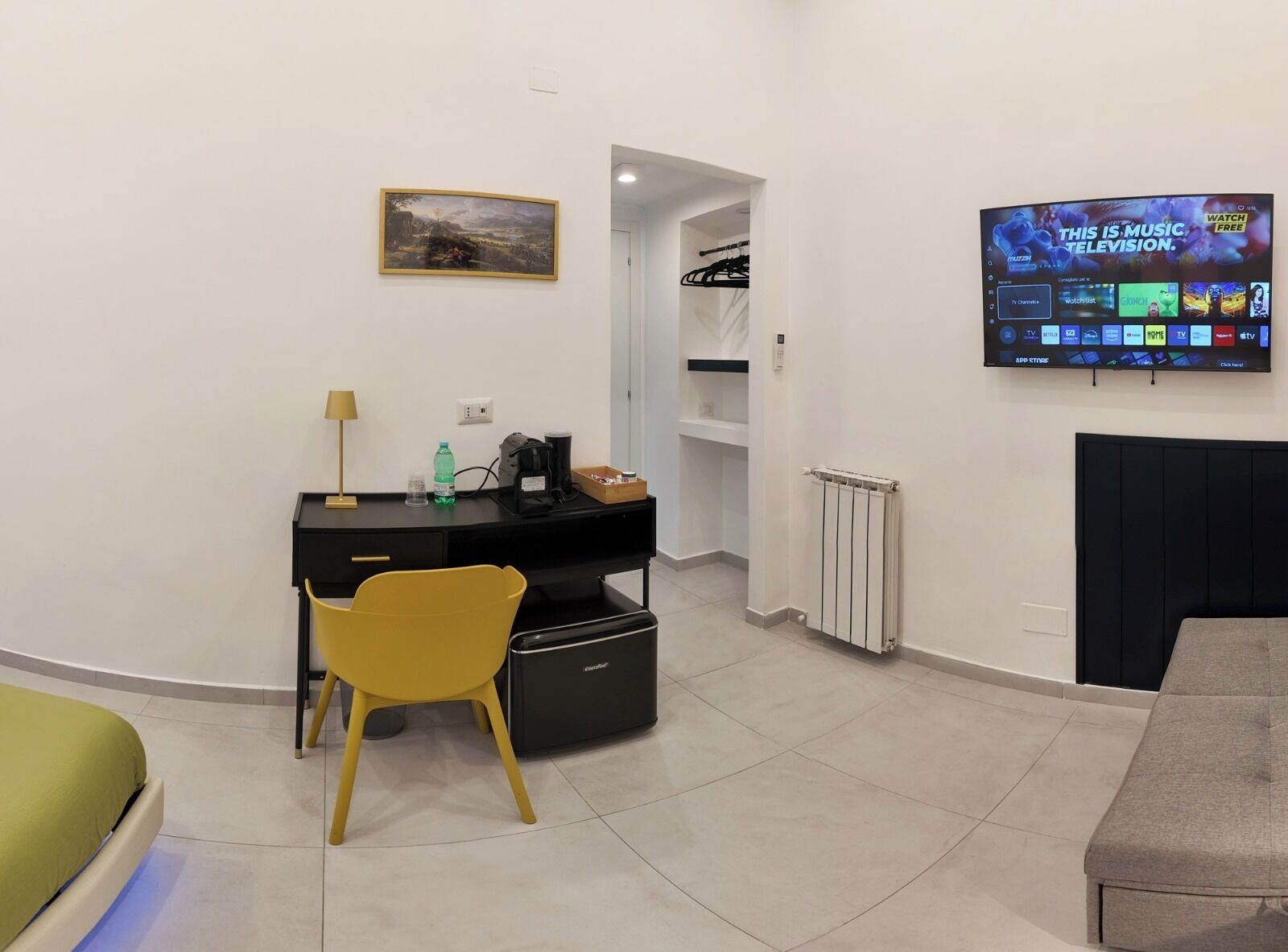 A modern living room with a black desk, a yellow chair, a TV mounted on the wall, and a fireplace.