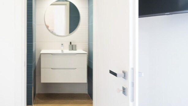 A modern bathroom with a white vanity, a round mirror, and a wooden floor. - Dimora Merliani (Naples)