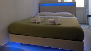 A modern bedroom with a bed, white linens, and a blue LED light strip under the bed. - Dimora Merliani (Naples)