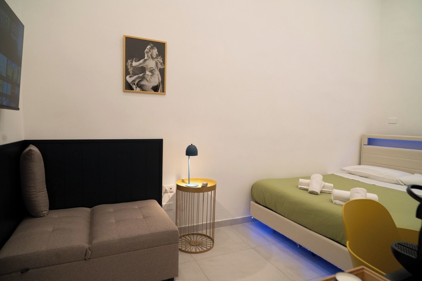Ein modernes Hotelzimmer mit Bett, einer Couch, einem kleinen Tisch mit Lampe und einem Bild an der Wand.