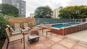 A rooftop pool area with lounge chairs and a small table, surrounded by a brick wall and a pool with a metal railing. - Your Complete Stay in a Building With a Pool and gym in the Best Location in Sao Paulo - Cars (São Paulo)