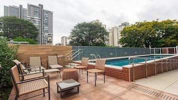 Uma área de piscina no terraço com espreguiçadeiras e uma pequena mesa, cercada por um muro de tijolos e uma piscina com grade de metal.