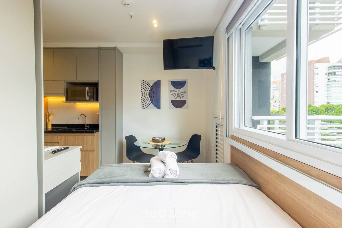 Una habitación de hotel moderna con cama, una mesita con sillas, un microondas en la kitchenette y cuadros en la pared.