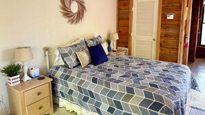A bedroom with a bed, nightstands, a dresser, a wall-mounted wreath, and a wooden door with a 'No Smoking' sign. - Blue Spirit · Private Studio Cabin in the Trees (Caddo Gap)