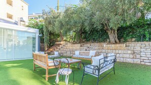 An outdoor patio with a stone wall, wooden furniture, and a large tree. - GlassHaus Rooftop 2-BR & Pool in Ghazir (Ghazir)