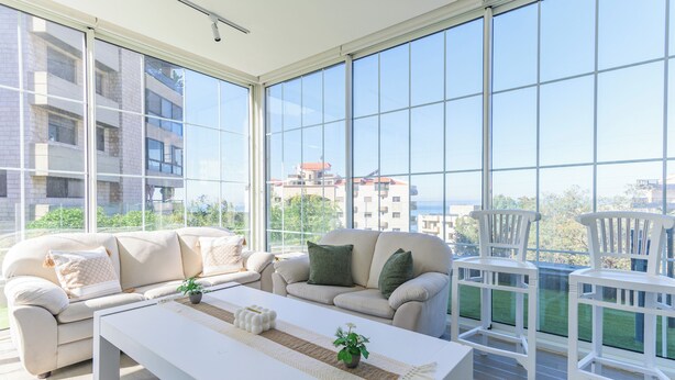 A modern living room with a large window, a sofa, a coffee table, and two white chairs. - GlassHaus Rooftop 2-BR & Pool in Ghazir (Ghazir)