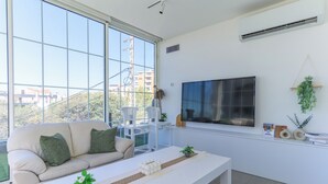 A modern living room with a large window, a flat-screen TV, a sofa, and a coffee table. - GlassHaus Rooftop 2-BR & Pool in Ghazir (Ghazir)