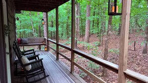 Une terrasse en bois avec un banc et une lanterne, donnant sur une forêt.