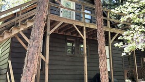 Une cabane en bois dotée d’un balcon dont la structure est soutenue par des arbres.