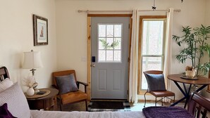 Une chambre confortable avec un lit, deux chaises, une petite table, une lampe et une porte avec des fenêtres.