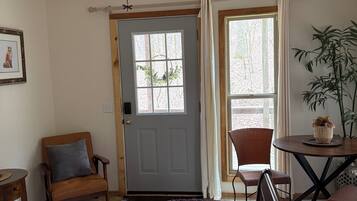 A room with a bed, a chair, a table, a ceiling fan, a door, and a window.