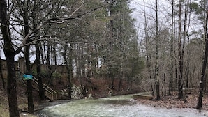Une rivière traverse une zone boisée, bordée d’une clôture en bois et d’un panneau indiquant « Cedar Creek ».