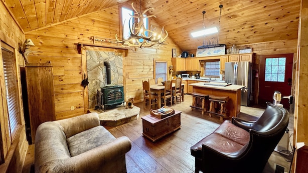 Interior acogedor de una cabaña con chimenea de piedra, muebles de madera y una zona de cocina.