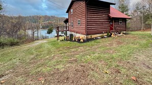 Una cabaña rústica con fachada de madera y techo rojo, ubicada junto a un lago con un muelle de madera que se adentra en el agua.