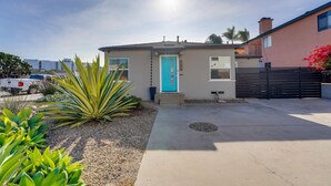 Una casa a un piano con una porta blu, un piccolo giardino anteriore con piante di agave e un'area di parcheggio con un veicolo bianco.