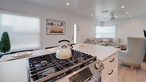 Una cucina moderna con piano cottura a gas, bollitore e tavolo da pranzo. Nell'area soggiorno adiacente, si trova un divano e una poltrona.