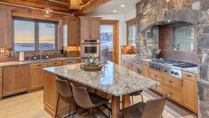 A spacious kitchen with a large island, wooden cabinets, a stone accent wall, and a view of the mountains. - The Wilson Vista: Epic Space & Solitude (Mountain Village)