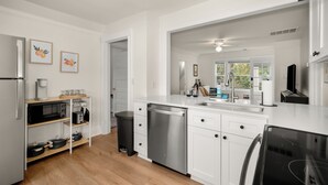 Una cocina moderna con armarios blancos, lavavajillas, microondas y cafetera sobre una repisa de madera.