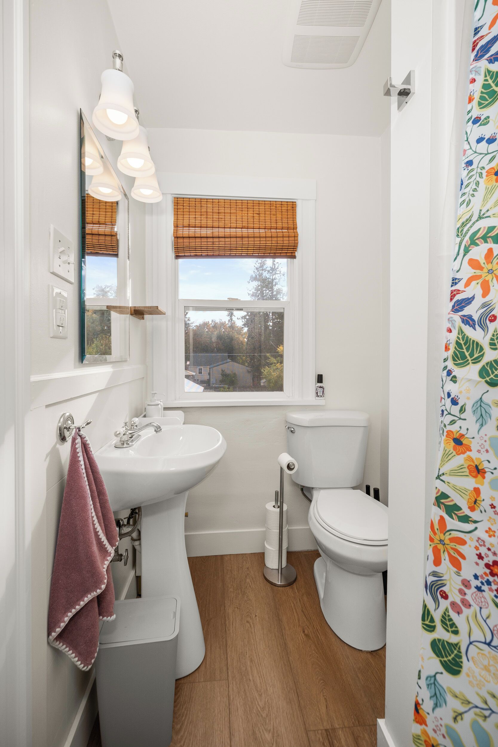 A small bathroom with a white sink, toilet, and window with blinds.