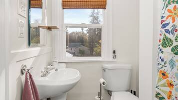 A small bathroom with a white sink, toilet, and window with blinds.