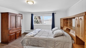 A bedroom with a bed, wooden wardrobe, and a window with curtains. - Lakefront Retreat w/ Dock + Games (Madison Lake)