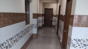 A hallway with tiled floors and walls, a wooden door at the end, and a window with bars on the left. - VIJETHA GRAND LODGE  (Mangalagiri)