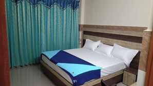 A bedroom with a bed, curtains, a nightstand, and a chair. - VIJETHA GRAND LODGE  (Mangalagiri)