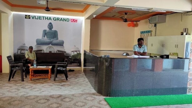 A reception area with a large Buddha statue, a reception desk, and a few chairs. - VIJETHA GRAND LODGE  (Mangalagiri)