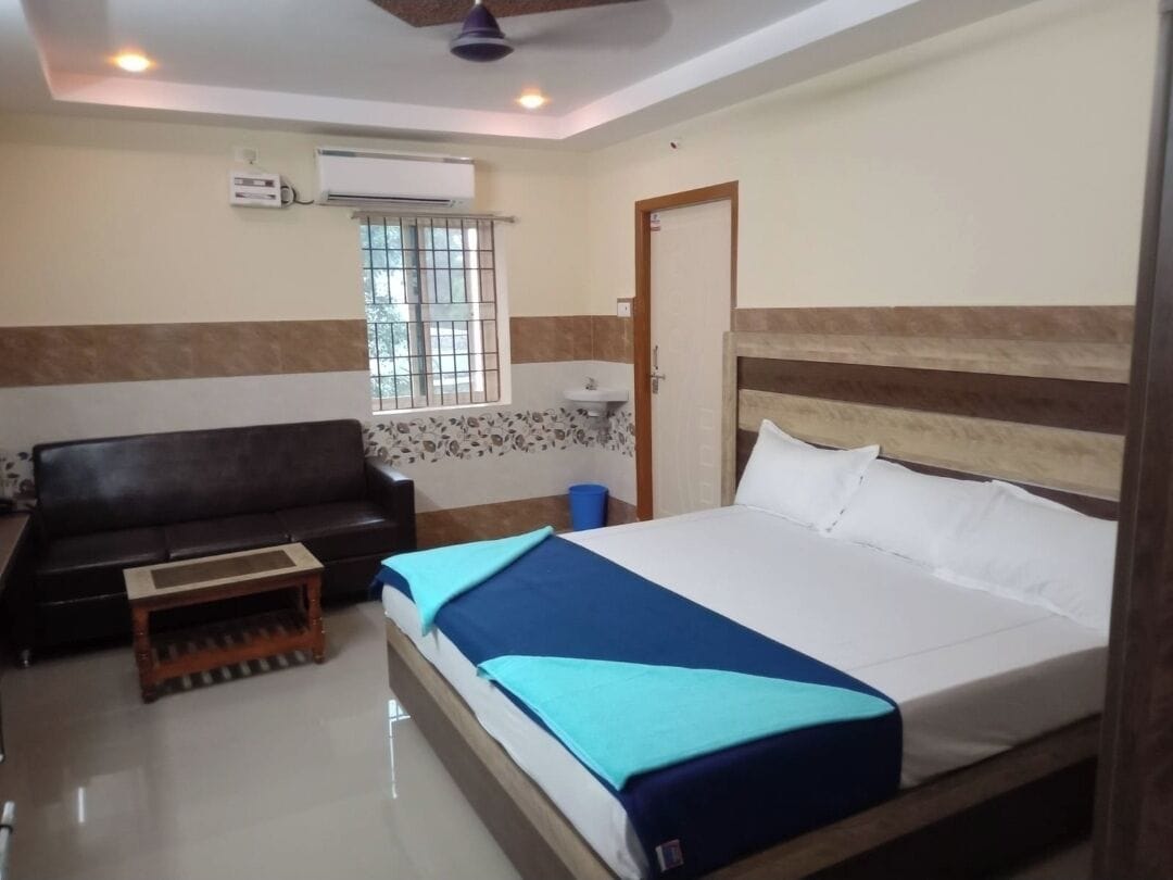 A bedroom with a bed, a sofa, a small table, a window, and a door.
